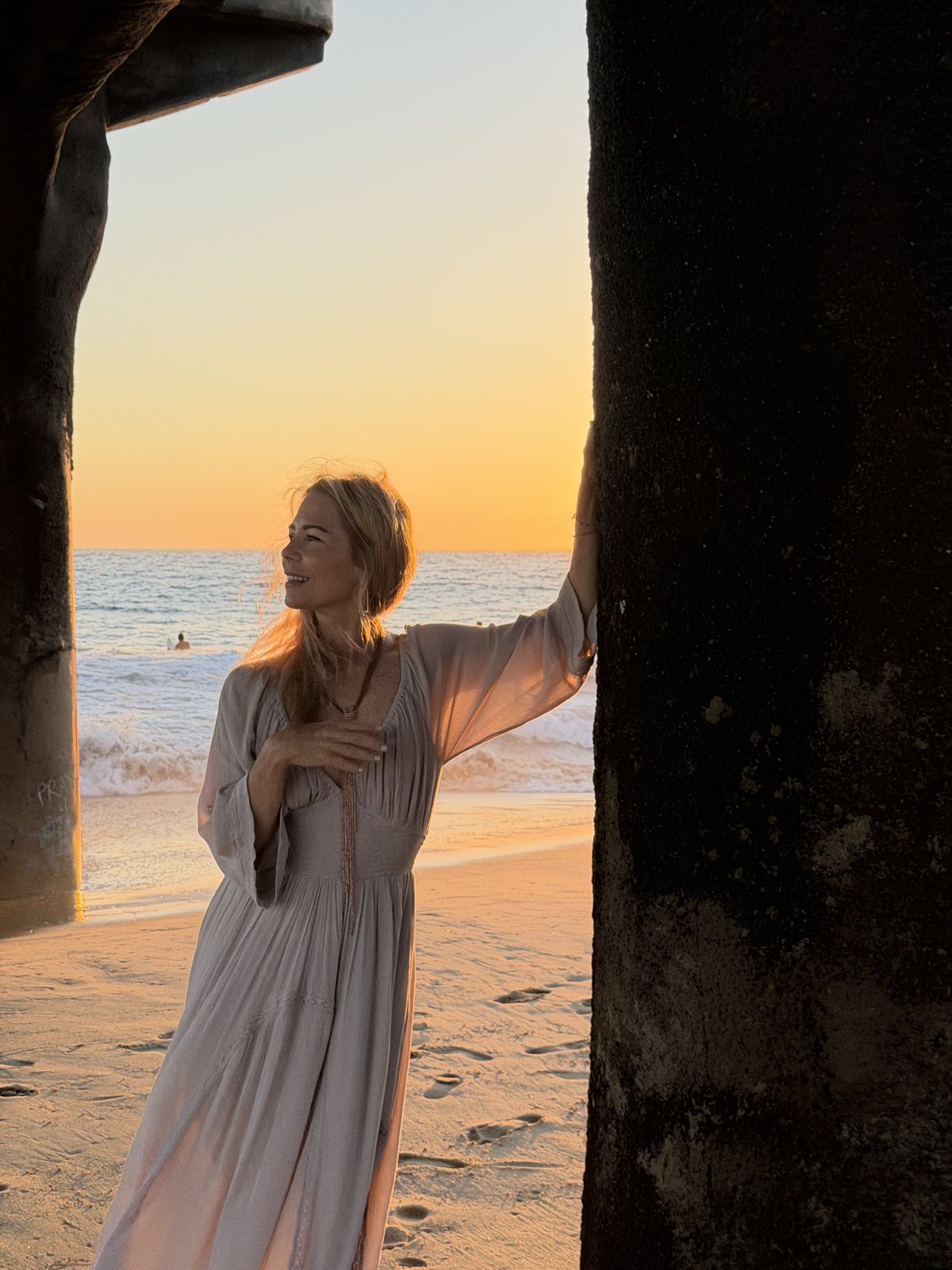 Christine Burke under a pier at sunset, looking out at the ocean